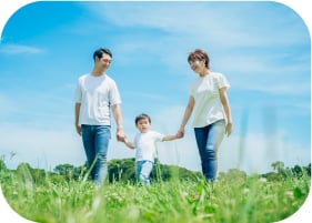 青空の下、緑の芝生の上で手をつないで歩く家族